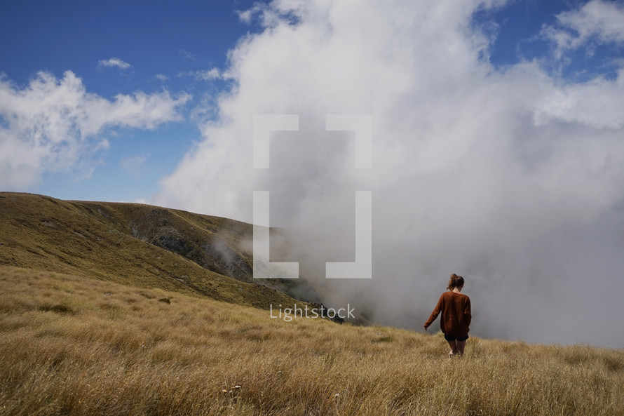 a woman walking through a field of tall grasses on a mountaintop in the clouds 