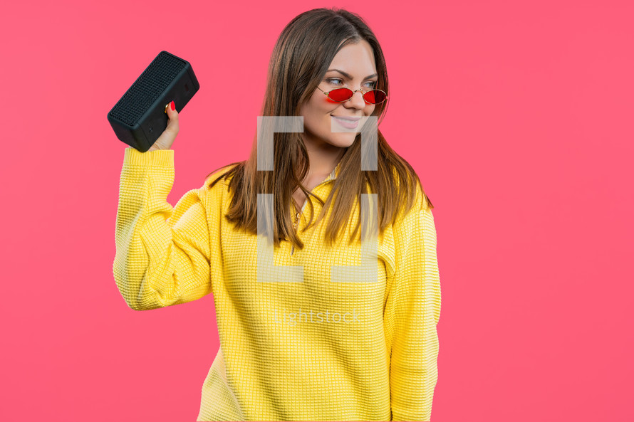 Lady dancing, enjoying on pink studio background. She moves to rhythm of music. Young woman listening to music by wireless portable speaker - modern sound system. . High quality photo