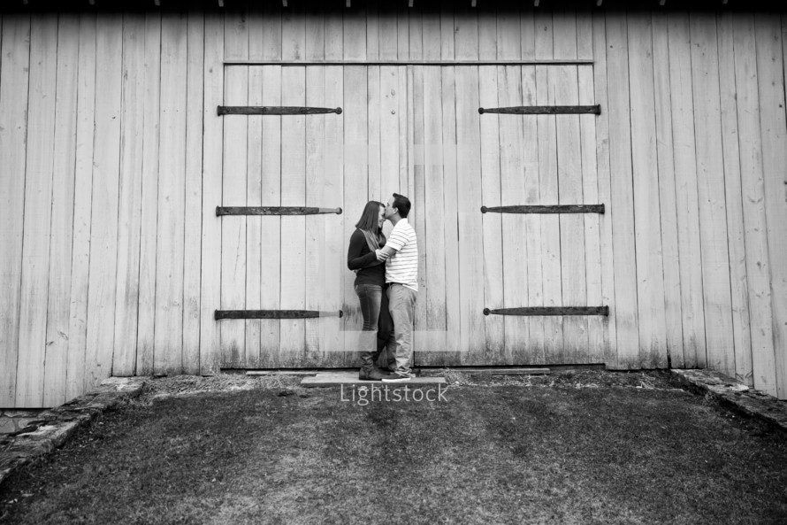 couple kissing in front of a barn 