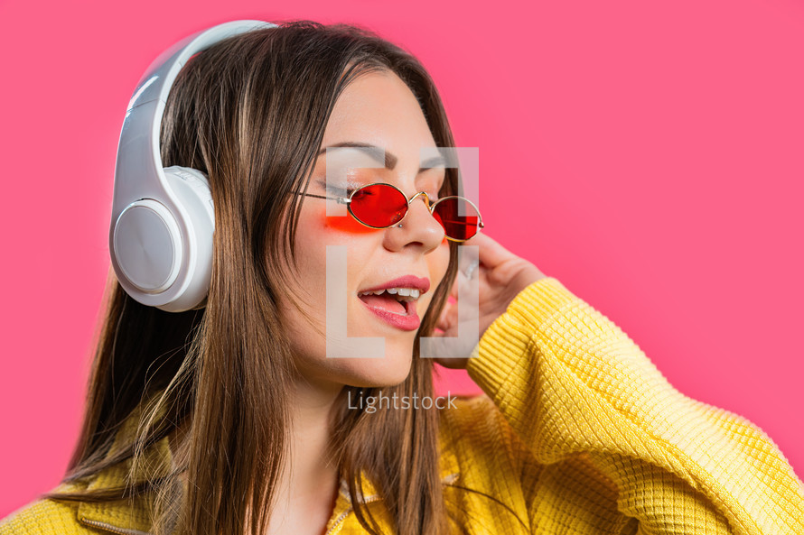 Positive woman listening music, enjoying with headphones on pink studio background. Radio, wireless modern sound technology, online player. High quality