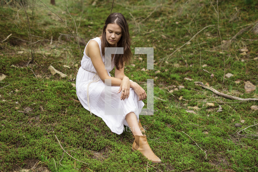 a young woman in dress siting on mossy ground 