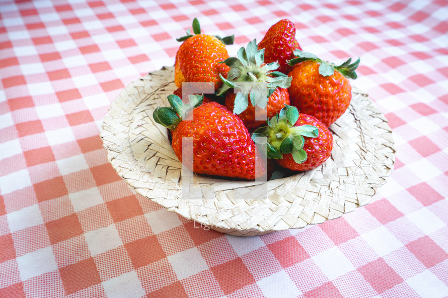 Fresh strawberries decorated on a straw hat. on a red picnic blanket.