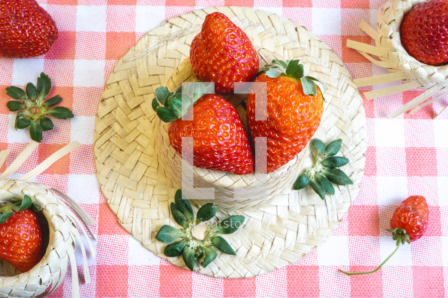 Fresh strawberries decorated on a straw hat. on a red picnic blanket.