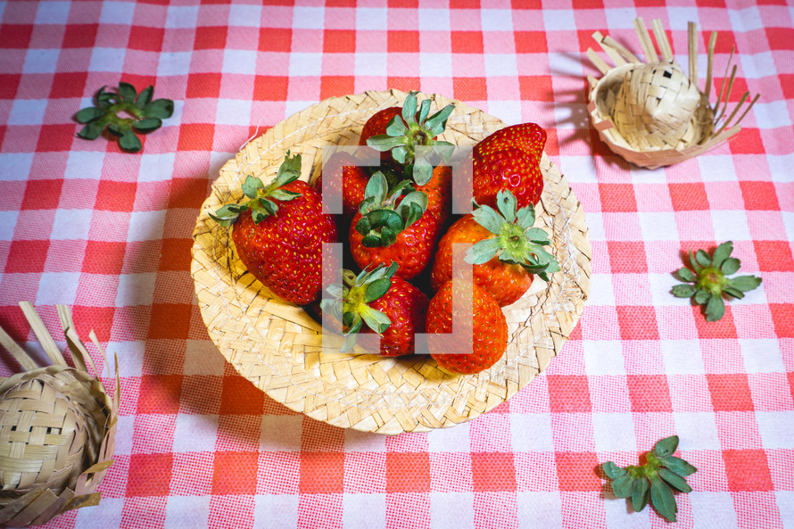 Fresh strawberries decorated on a straw hat. on a red picnic blanket.