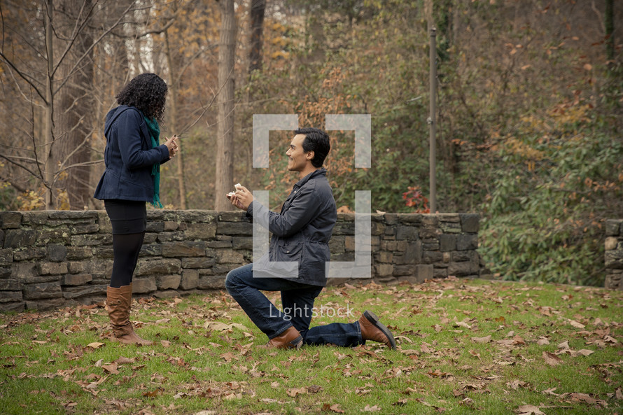 man on one knee proposing to a woman outdoors