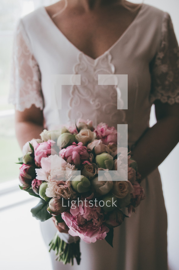 a bride holding a bouquet standing in a window 