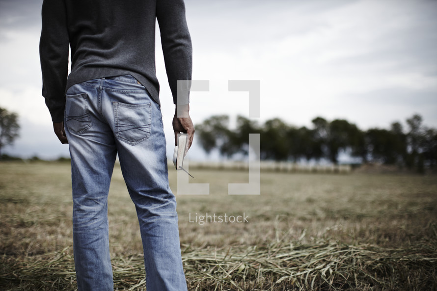 Man standing in a field holding his bible