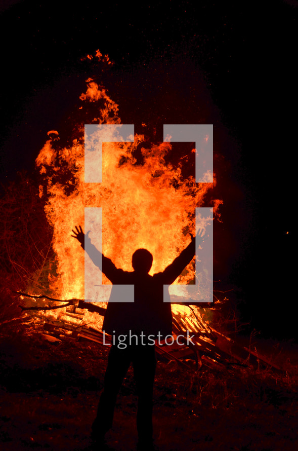 man with his hands raised in front of a burning bonfire