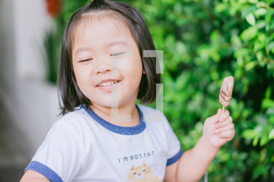 a toddler girl eating chocolate ice cream on a stick 
