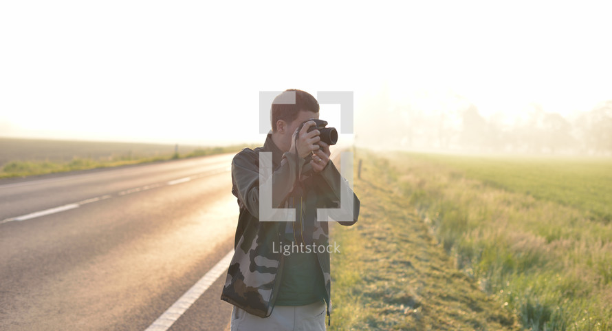 Landscape professional photographer taking a picture near a road with the sunrise in the background