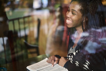African American woman reading a Bible sitting in a window seat in a coffee shop 