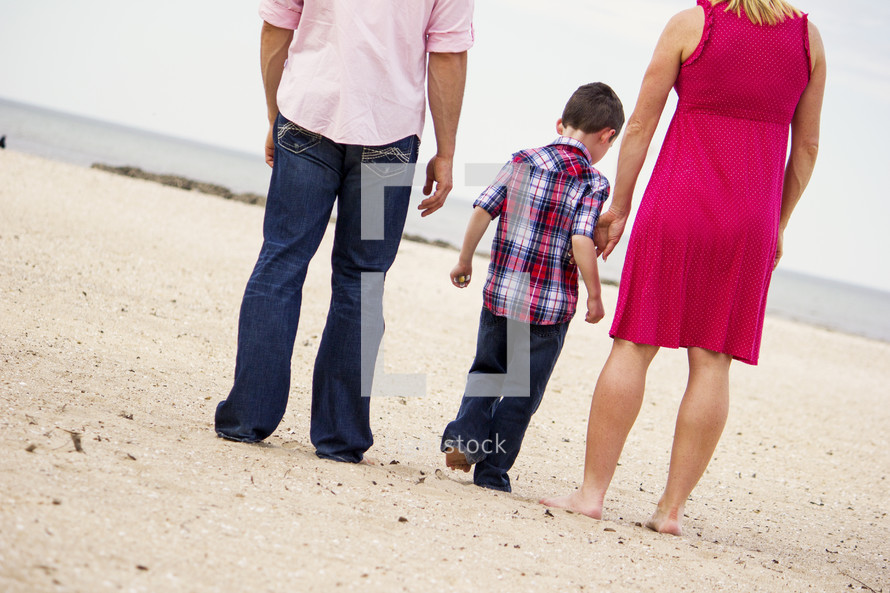 Back view of father, boy and mother walking on white beach
