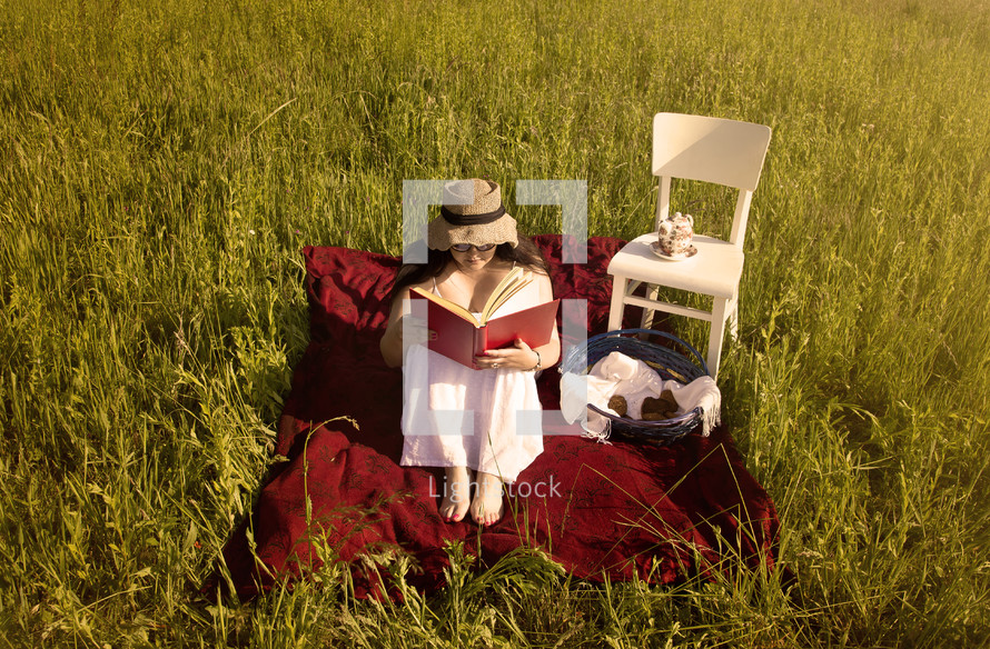 a woman reading a book on a blanket in the grass