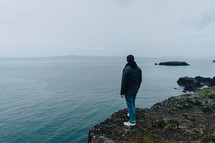 man standing at the edge of a cliff looking out into the ocean 