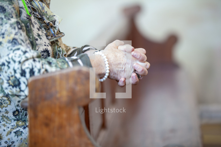 elderly woman's praying hands over a pew 