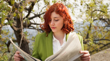 Red hair businesswoman reading newspaper under the tree