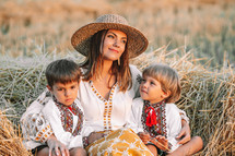 Beautiful ukrainian family - woman and sons in vyshyvanka shirts lying on hay in countryside at sunset. Nature, haystack, vacation, relax and harvest concept. Children, family fun, love