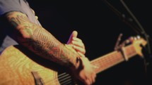 Hands holding an acoustical guitar near a microphone.