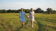 Friendly family. Mother and daughter holding hands at sunset running in the meadow. Happy mom and daughter walk holding hands towards the sunset in summer. Freedom happiness concept.
