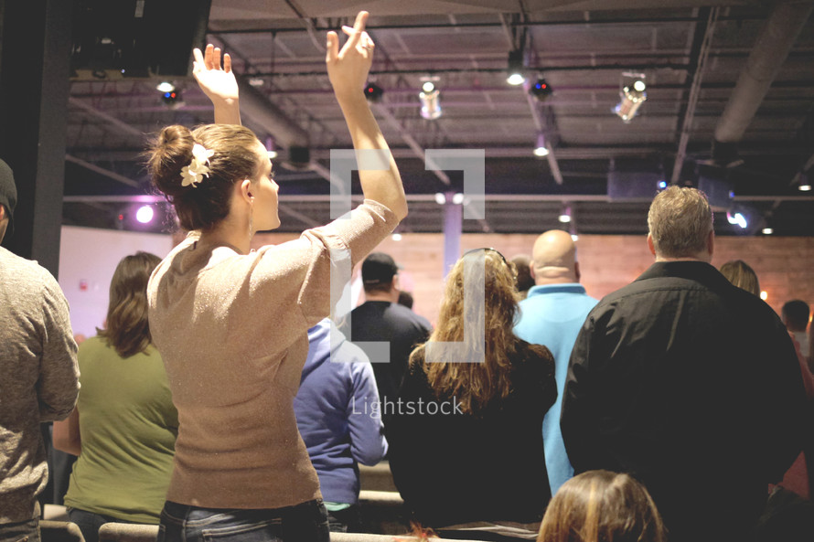 A woman raises her hands in praise at a church service.