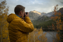 man with a camera standing near a lake in fall 