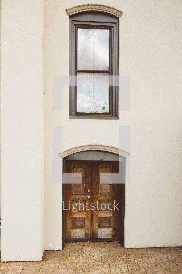 Wooden doors and a window in the front of a stucco building.