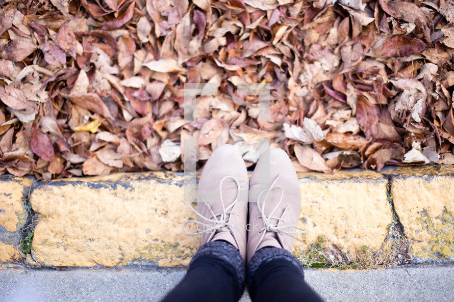 Feet on the curb with autumn leaves.