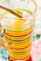 A striped pitcher full of lemonade wood spoon