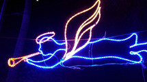 A neon blue and white Christmas Angel decoration lights up the night sky to blow a trumpet and announce the birth of Jesus.
