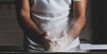 Man kneads raw dough, dust from flour