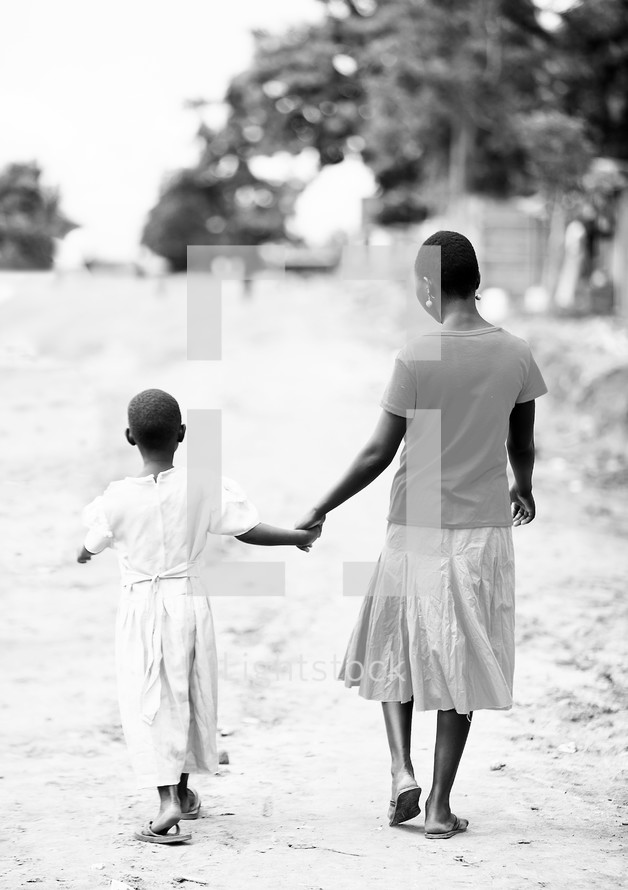woman and girl holding hands and walking on a dirt road