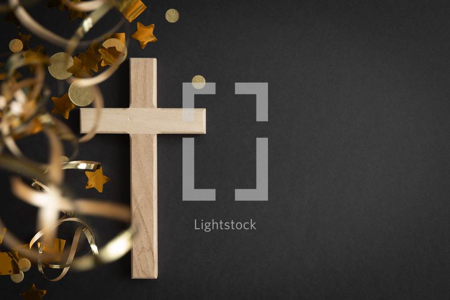 Wood cross with gold streamers and confetti on a black background with copy space