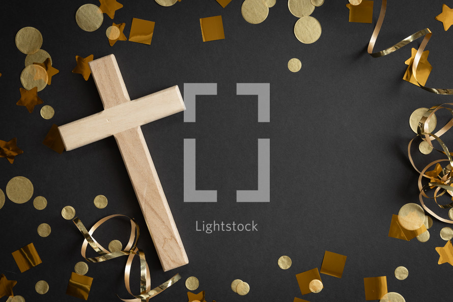 Wood cross with gold streamers and confetti on a black background with copy space