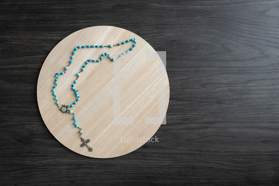 Blue rosary on a round wood tray with a dark background