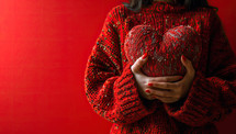 A woman in a red sweater holds a heart on a red background