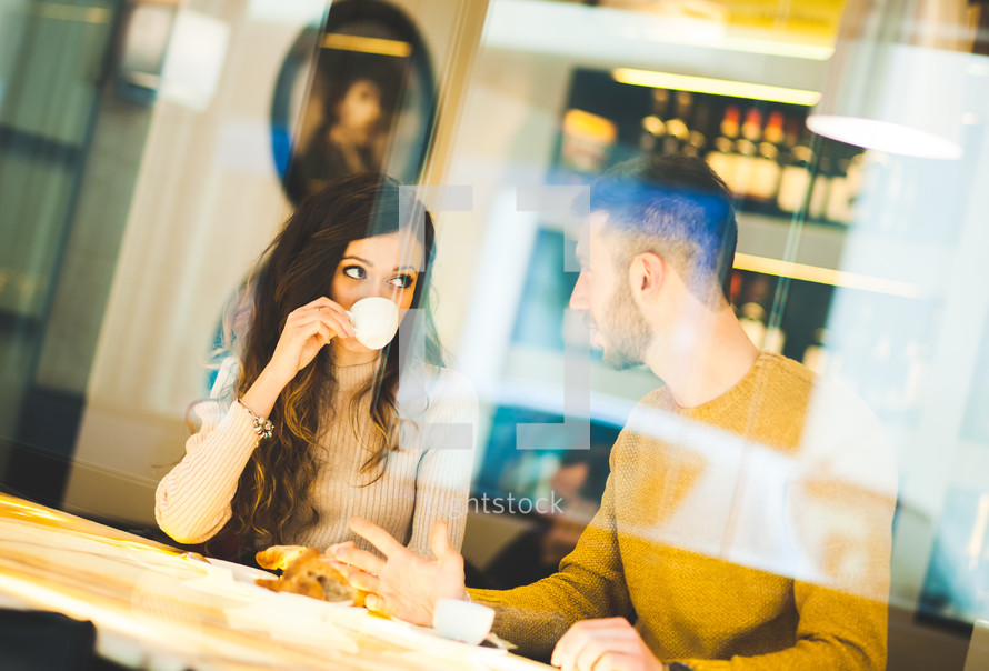 Young couple at a coffee shop drinking an italian espresso. Reflection view from outside.