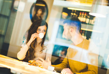 Young couple at a coffee shop drinking an italian espresso. Reflection view from outside.