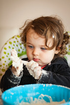 Little baby girl playing with dough on the high chair.