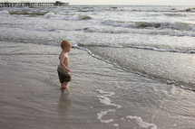 A little boy wades in the ocean.