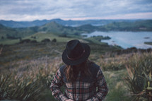 a man in a plaid shirt and hat standing on mountain top 