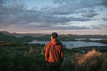 a man in a jacket standing on a mountaintop at dawn 