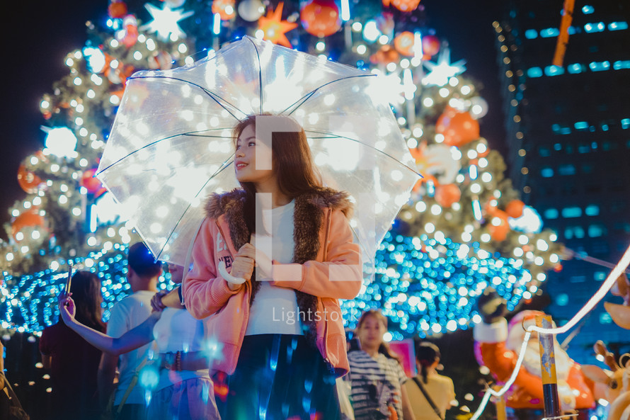 a woman holding an umbrella standing in front of a Christmas tree