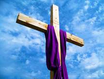 A purple shroud draped over a cross against a blue sunny sky signifying that Jesus is not here but Risen from the Dead, showing the glory of the resurrected Jesus from the dead. The Cross is our symbol of hope showing that death can not hold the King of Kings and the author of all life. 