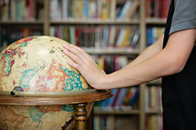 Hands on a world globe in a library.
