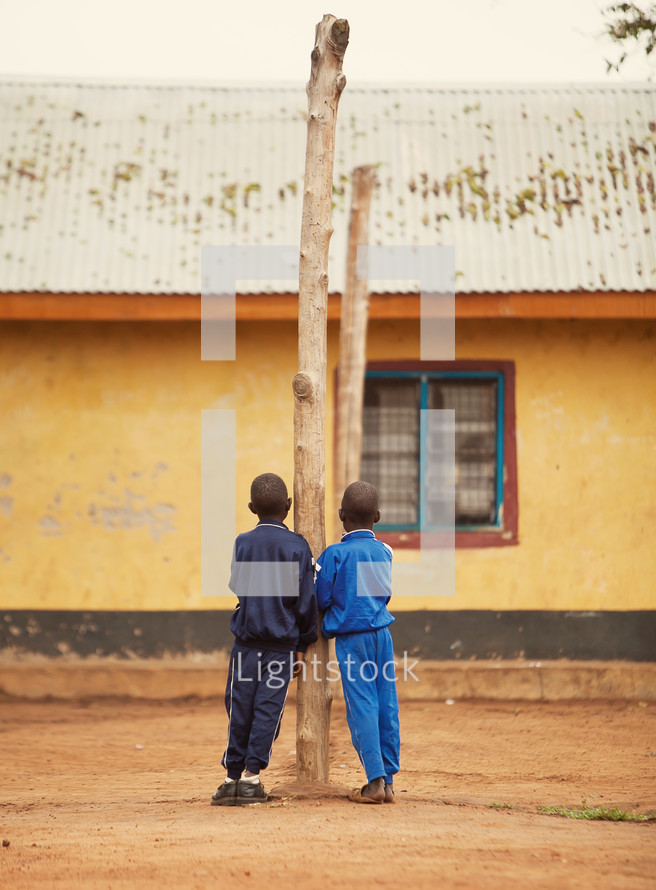 two young boys leaning on a tree trunk