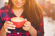 a woman in a plaid shirt holding a latte 