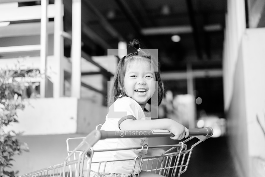 a toddler girl sitting in a shopping cart 