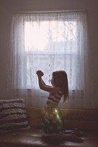 girl child with praying hands in front of a window 