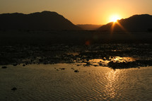 sunset behind mountains and reflection over water along a shore 