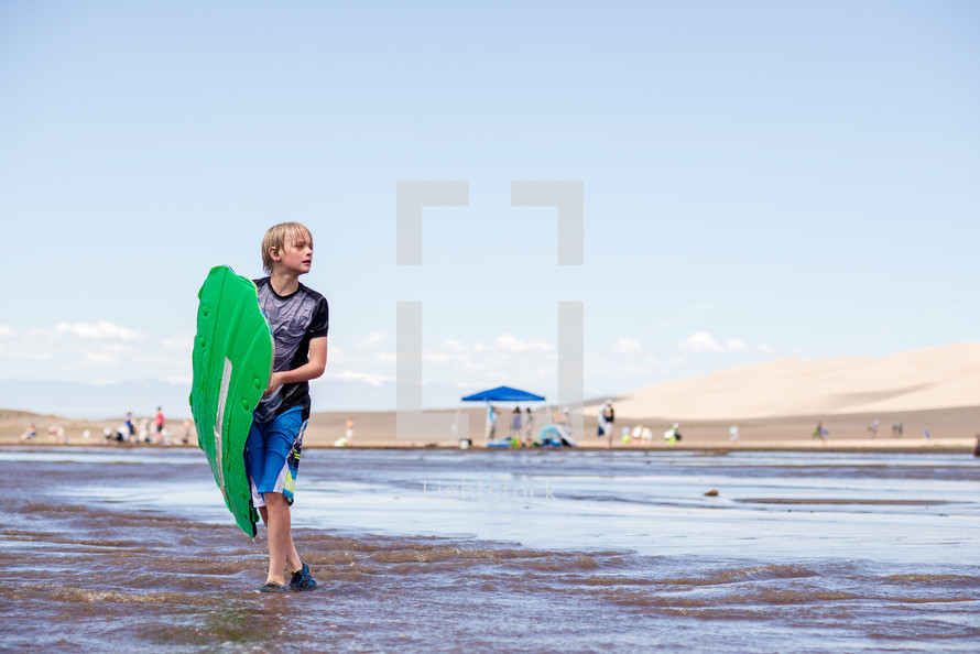 a boy child with a boogie board walking on a beach